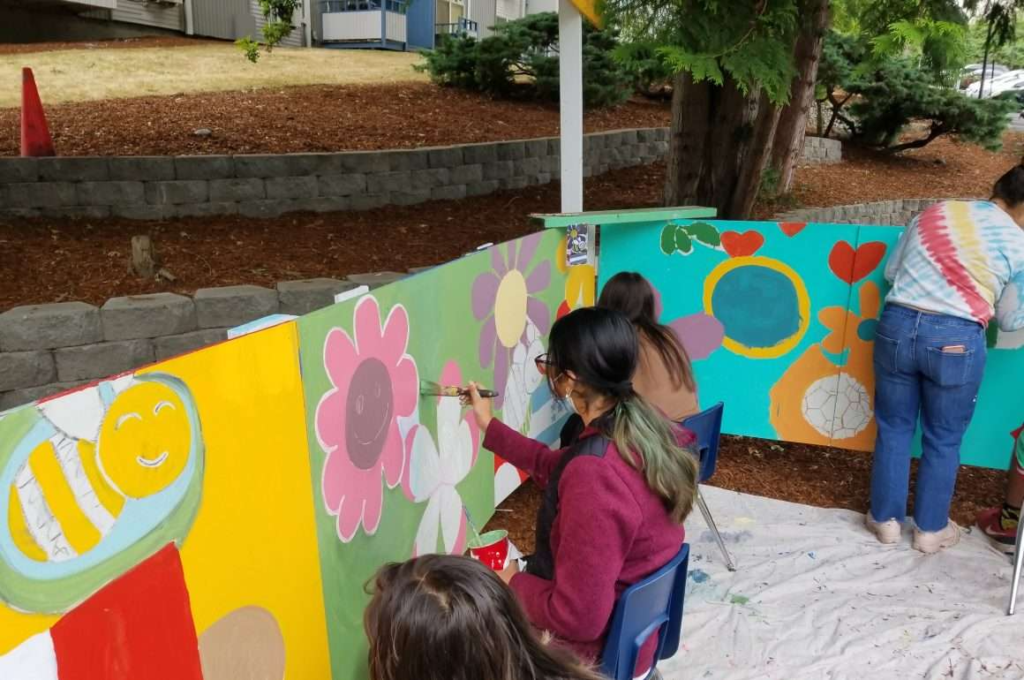 volunteers paint a mural on a fence